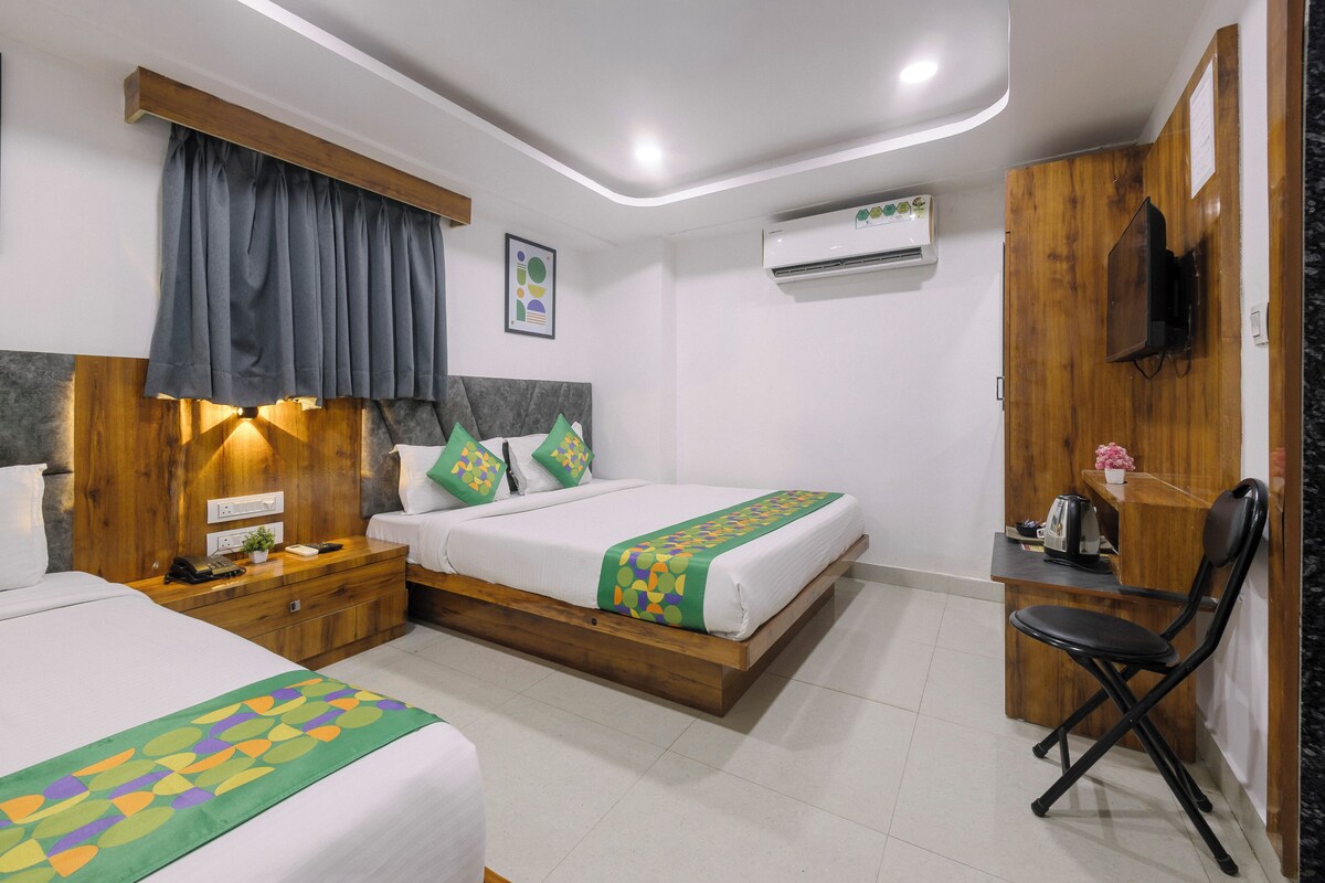 A hotel room with two beds, a desk, a chair, and a TV.