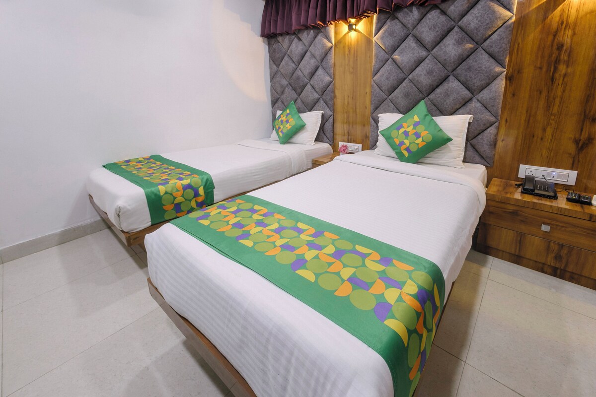 A hotel room with two beds, each with a green and white bedspread, a wooden headboard, and a nightstand with a phone.
