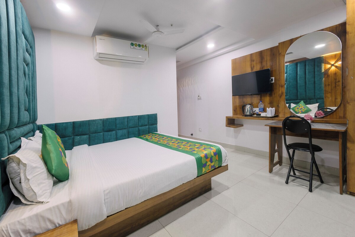 A hotel room with a bed, a desk, a chair, a TV, and an air conditioner.
