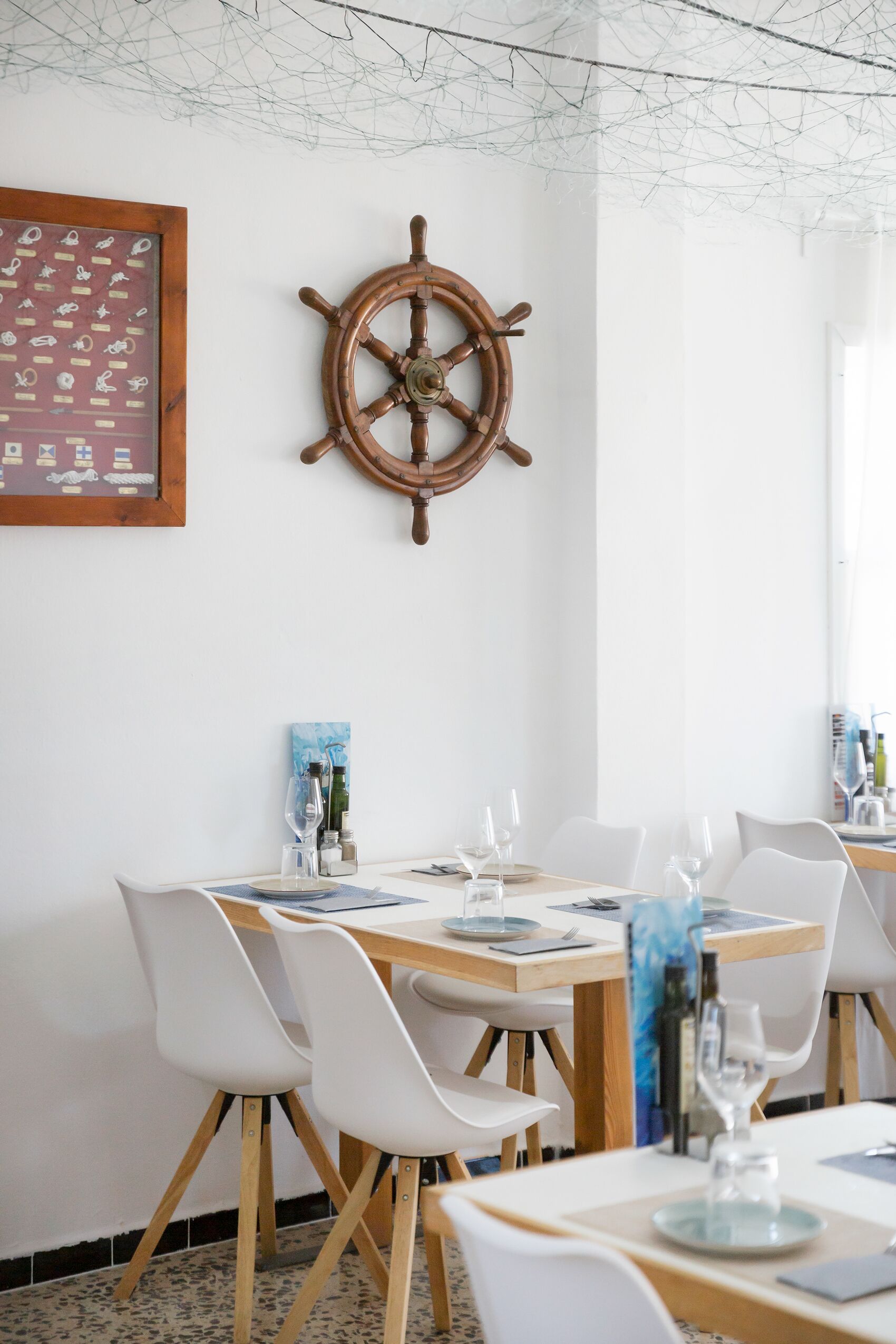 A dining area with a wooden table, white chairs, and a ship's wheel decoration on the wall.