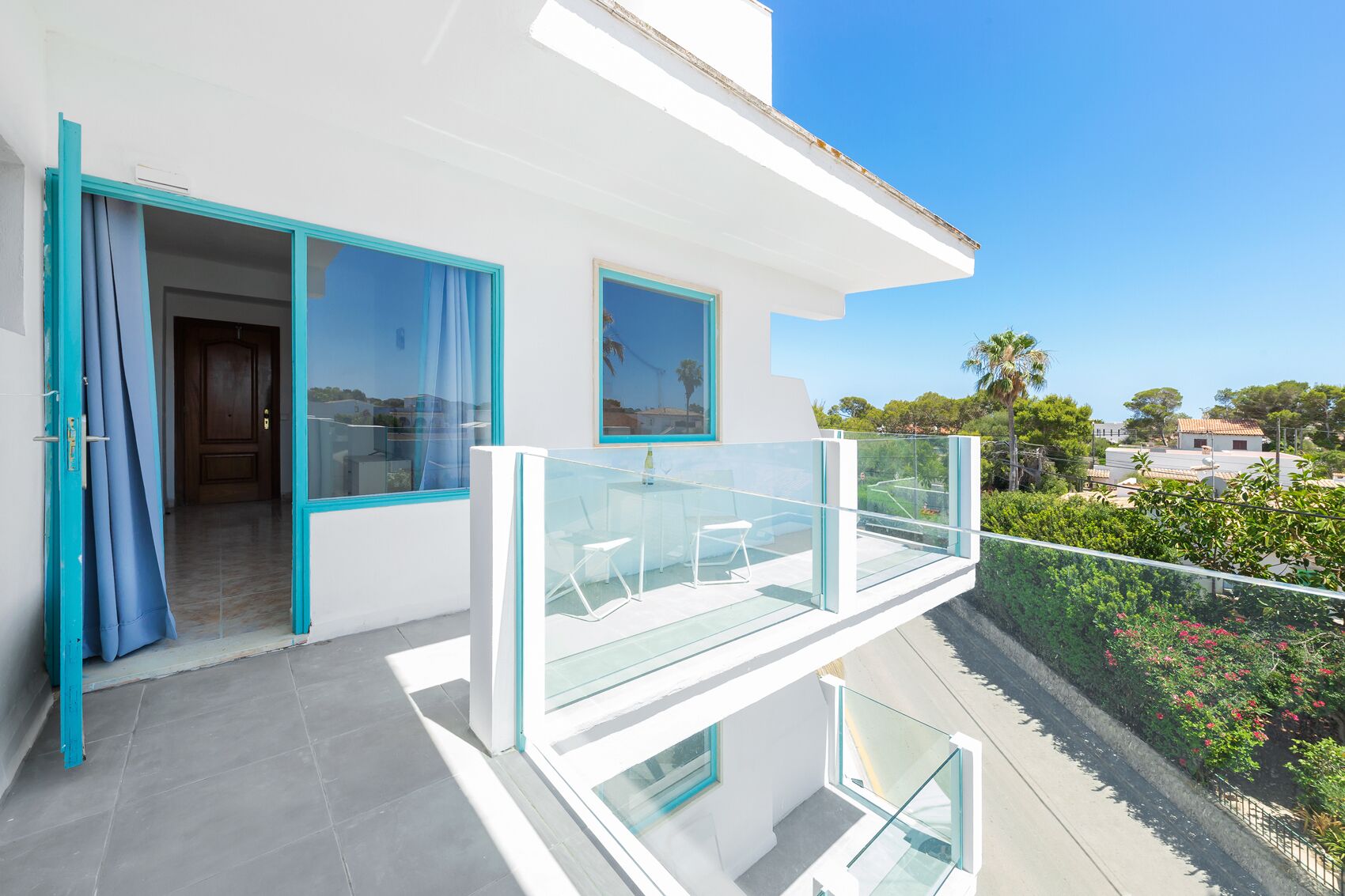 A modern house with a balcony, a door with blue curtains, and a view of the neighborhood.