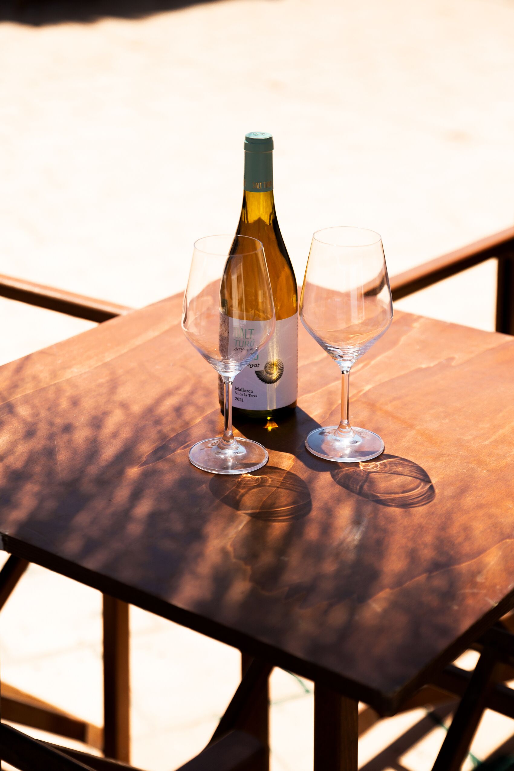 Una botella de vino y dos copas sobre una mesa de madera al aire libre.