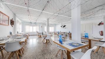 A spacious dining area with multiple tables and chairs, a high ceiling with exposed wiring, and a world map on the wall.