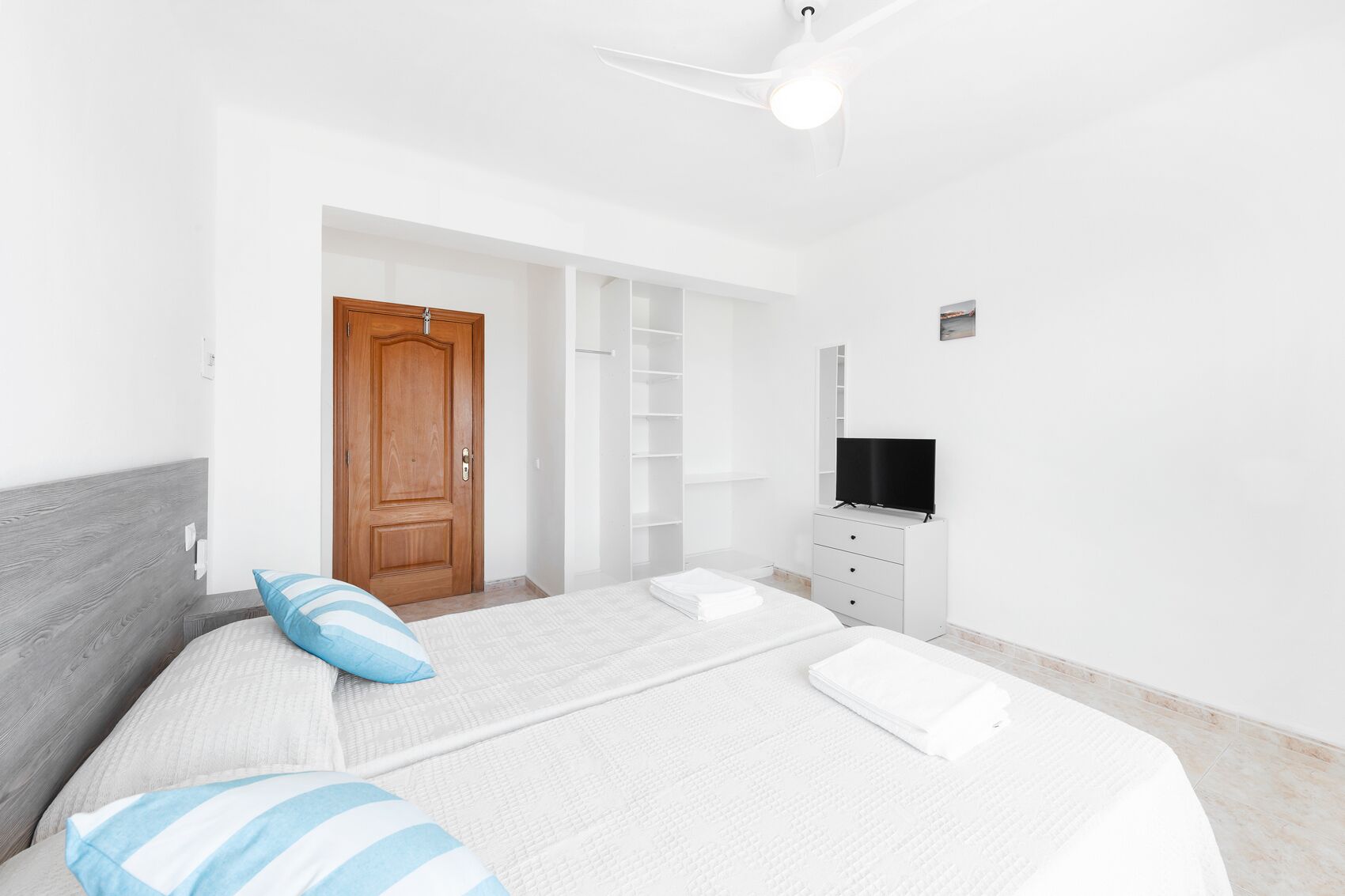 A bedroom with two beds, a wardrobe, a TV, and a ceiling fan.