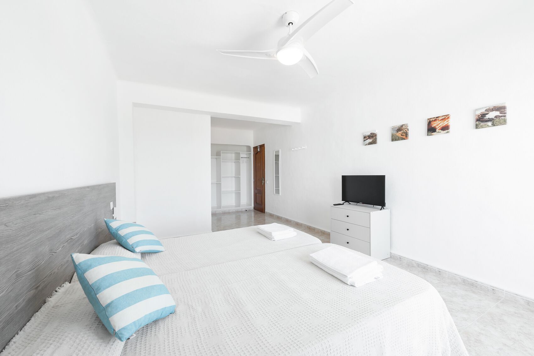 A modern bedroom with a large bed, a TV on a white dresser, and a walk-in closet.