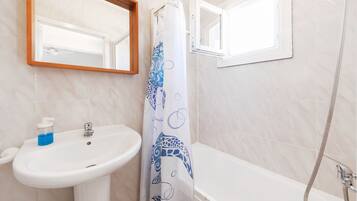 A bathroom with a white sink, a mirror, a shower, and a window.