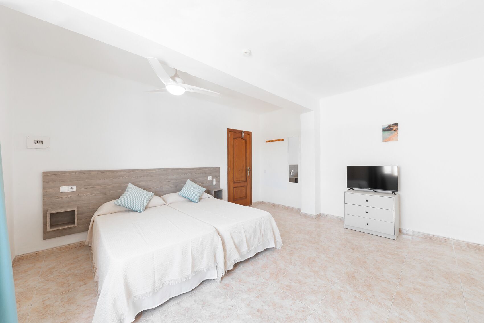A bedroom with a bed, a TV, a wardrobe, and a ceiling fan.