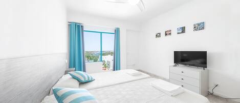 Una habitación de hotel moderna con dos camas, un televisor y un balcón con cortinas azules.