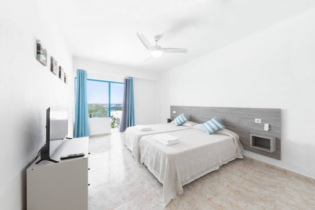 Una habitación de hotel moderna con una cama grande, un escritorio con una computadora y vistas a la ciudad.