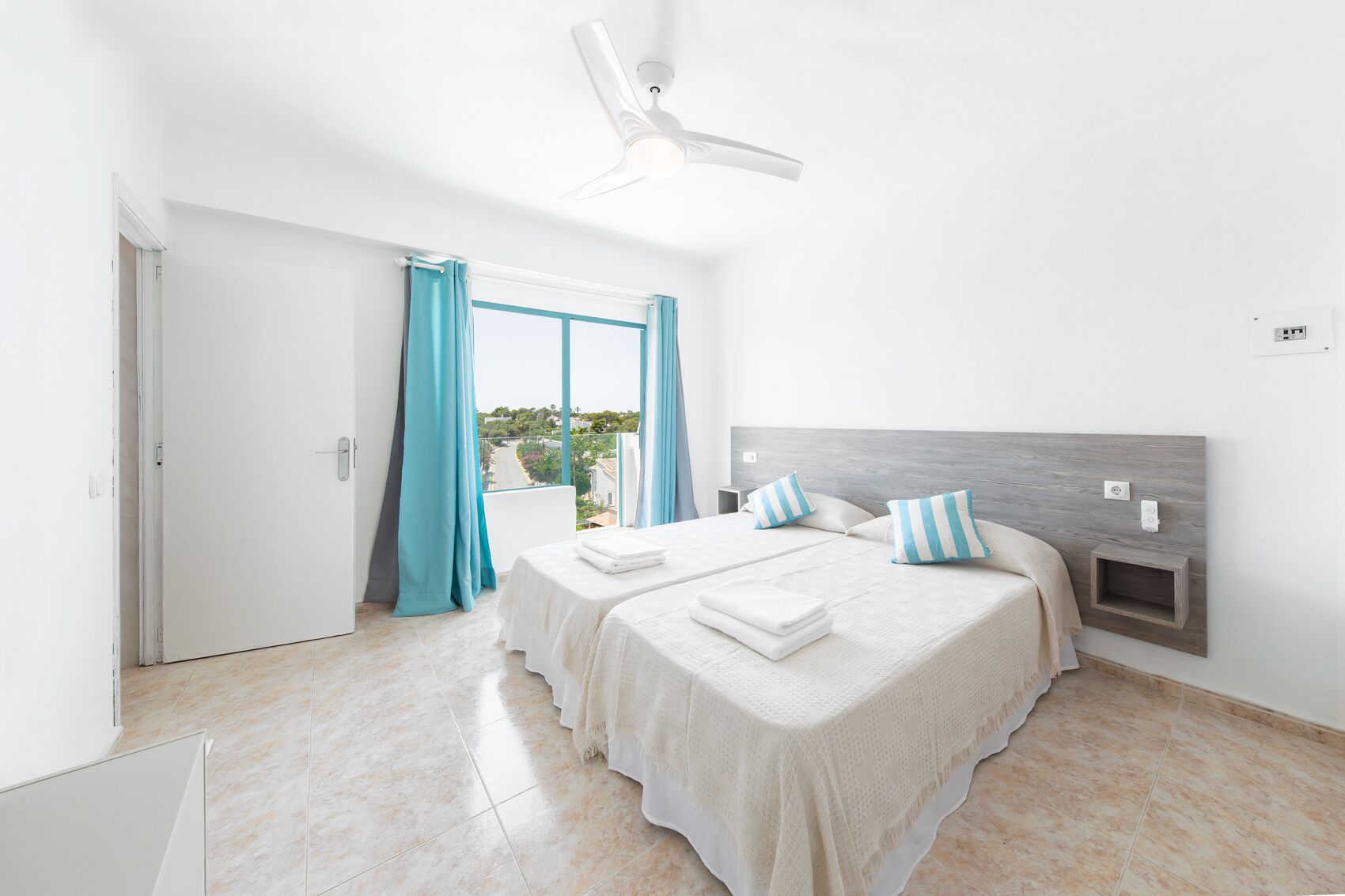 Habitación de hotel con una cama grande, ventilador de techo y vistas al exterior.