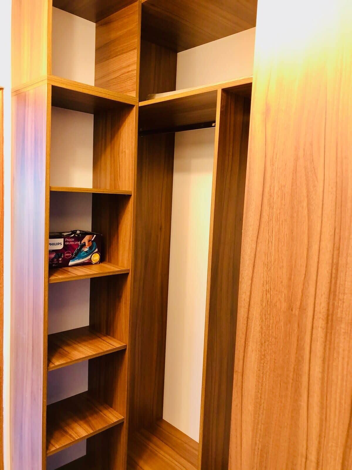 Une étagère en bois, dotée de plusieurs compartiments, dont certains contiennent des objets tels qu’un appareil de la marque Philips.