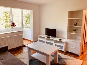 A modern living room with a white TV stand, a flat-screen TV, a white table, and a bookshelf.