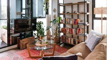 Relax in this inviting living room with a sofa, coffee table, and bookshelf, surrounded by large windows.