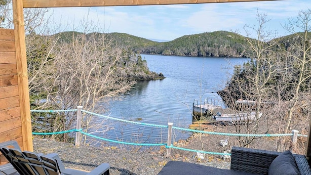 Una terraza de madera con mobiliario exterior, vista a un lago y un paisaje boscoso.