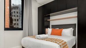 A modern hotel room with a large bed, a window with a city view, and built-in black cabinets. - Cozy Studio by Table Mountain Explore Cape Town (Cape Town)