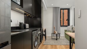 A compact kitchen with modern appliances, a dining area with a small table and chairs, and a view of a brick building through a window. - Cozy Studio by Table Mountain Explore Cape Town (Cape Town)