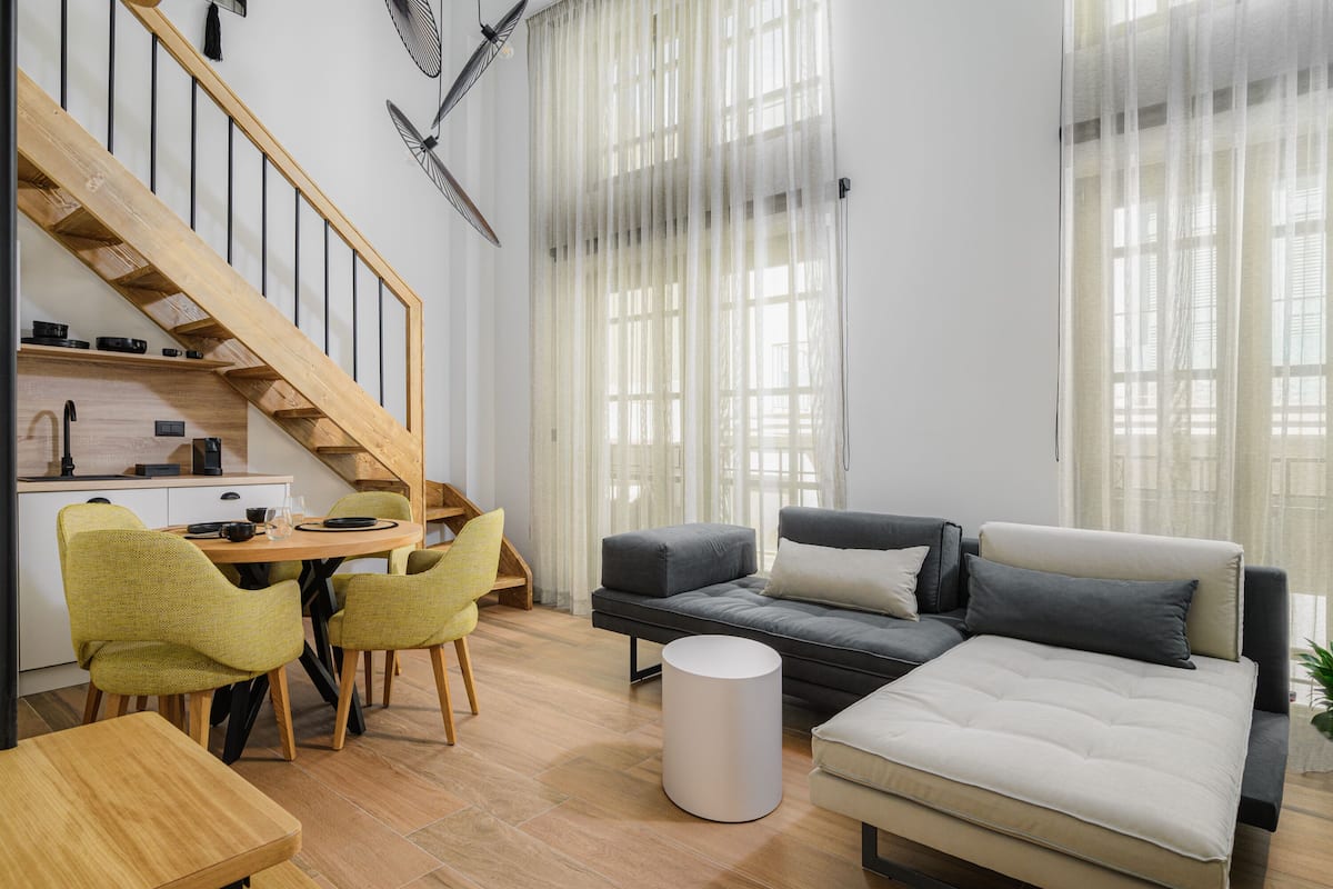A modern living room with a wooden staircase, a dining area with chairs, a sofa, and a round coffee table.