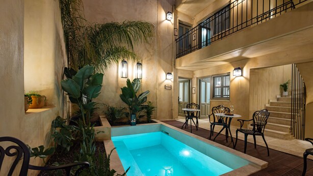 Uma área de piscina com uma piscina retangular, cercada por vasos de plantas e móveis de exterior.