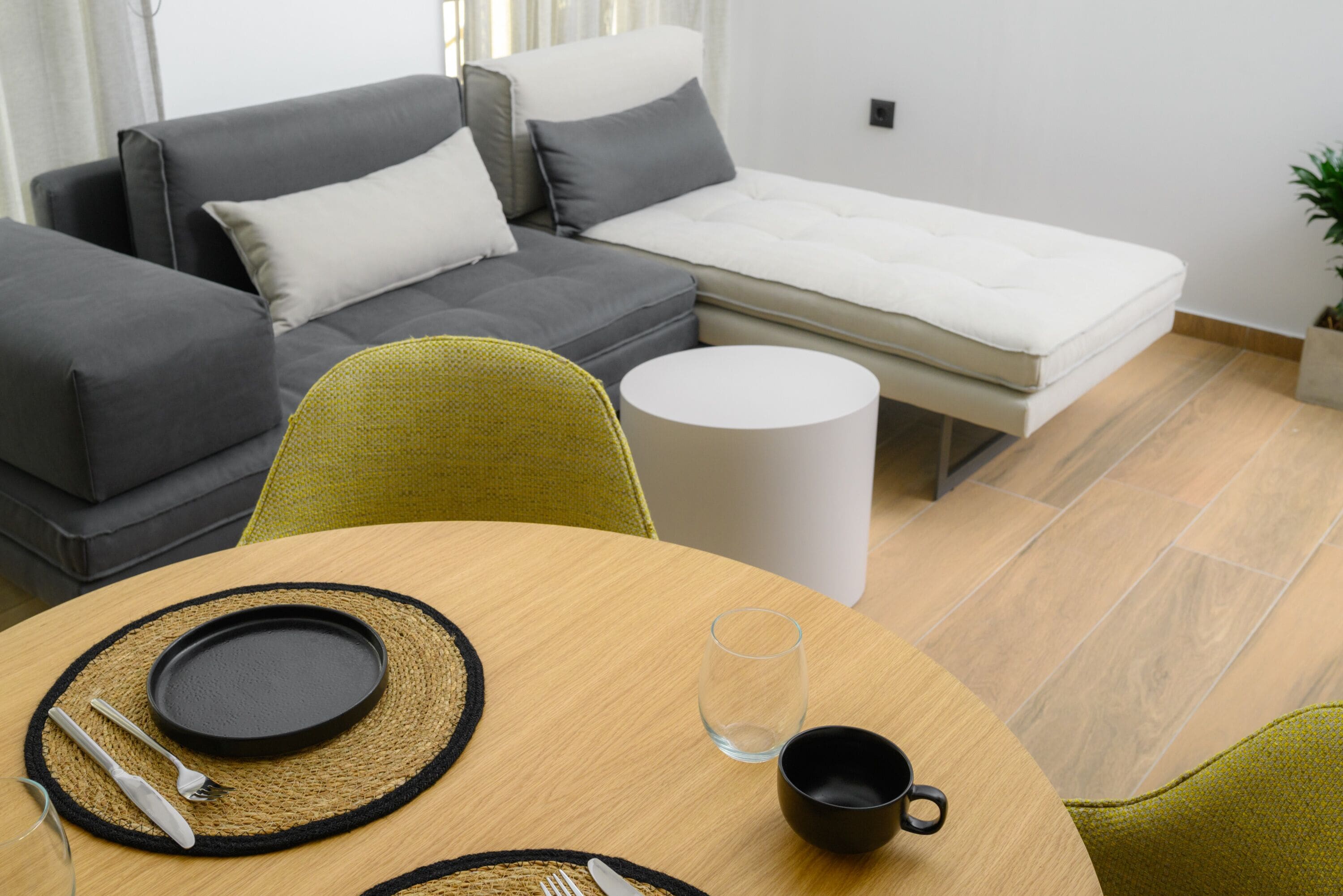 Una sala de estar moderna con un sofá, una mesita con mantel individual, cubiertos y una copa.