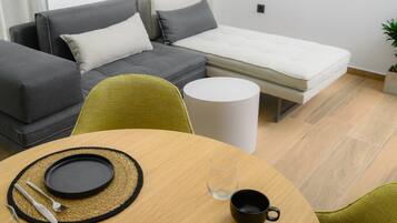 Una sala de estar moderna con un sofá, una mesita con mantel individual, cubiertos y una copa.