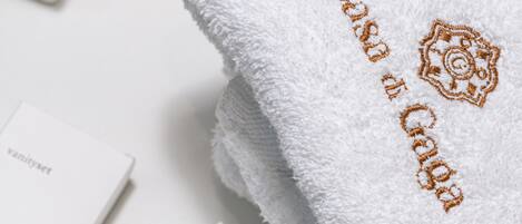 A white towel with embroidered text and a logo, two bottles of toiletries, and a black bowl on a white surface.