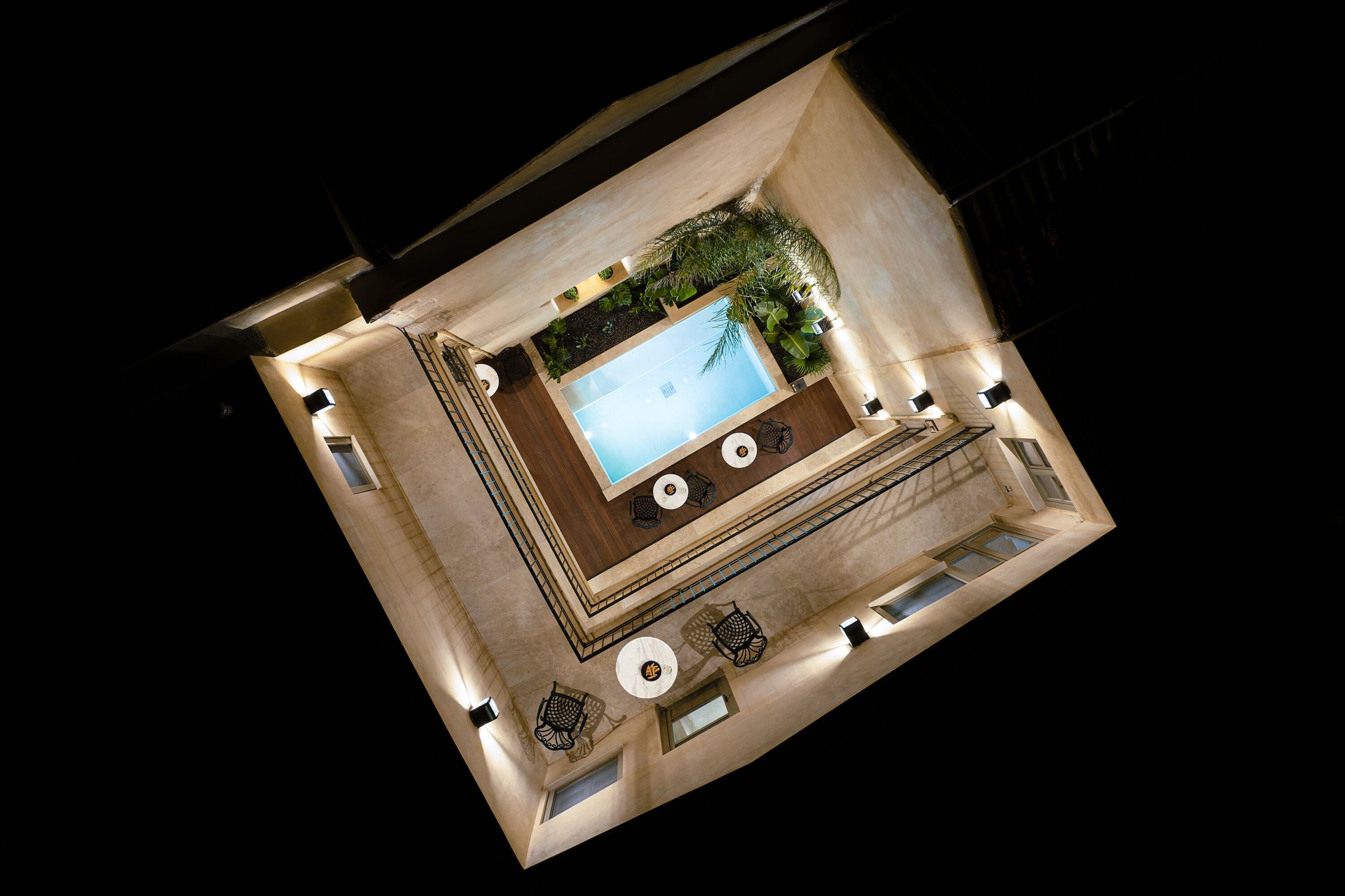 A top-down view of a pool area with a rectangular pool, surrounding lounge chairs, and a small seating area with a table and chairs.