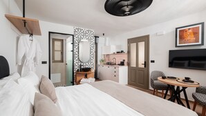 Quarto de hotel moderno com uma cama grande, uma kitchenette pequena, um espaço de refeições e uma televisão.