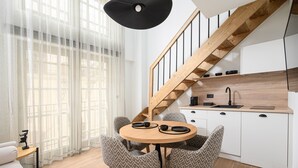 Uma cozinha moderna com escada de madeira, uma mesa de jantar redonda com cadeiras estampadas e um sofá branco em um ambiente claro com cortinas leves.
