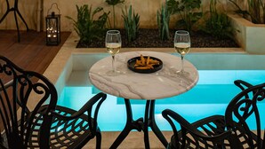 Área de refeições à beira da piscina, com uma mesa, cadeiras e dois copos de vinho branco.
