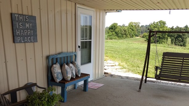 A covered porch with a blue bench, a table with a potted plant, and a swing set. - MY HAPPY PLACE - view of Ark from our farm (Williamstown)