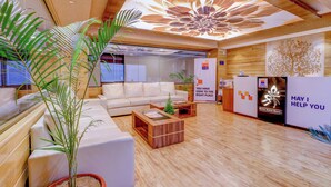 A modern hotel lobby with a wooden floor, white sofas, a reception desk, and a large floral ceiling design.