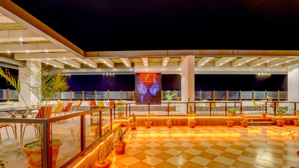 A rooftop terrace with a checkered floor, potted plants, and a large illuminated sign.