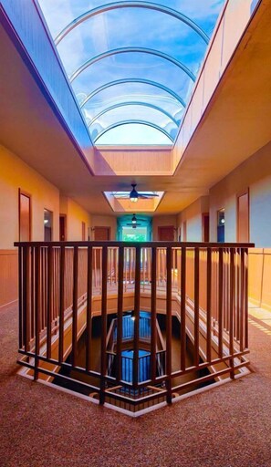 A hotel corridor with a central atrium, a glass ceiling, and a wooden railing. - IC 316 Riverfront Bliss (New Braunfels)