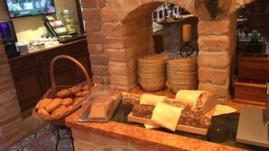 Un comptoir de boulangerie avec du pain et des pâtisseries, un téléviseur diffusant une scène, et un mur de pierre orné d’une plante suspendue.