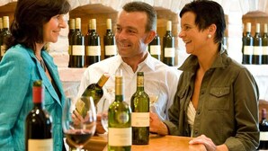 Trois personnes sont debout au bar, avec des bouteilles de vin en arrière-plan.