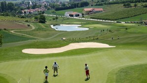 Un parcours de golf avec un étang, des bunkers de sable et une église en arrière-plan.