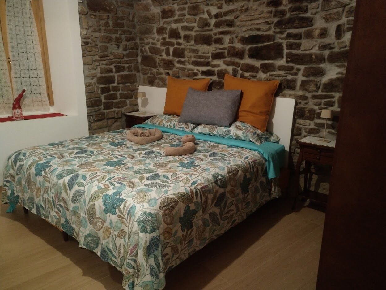 A bedroom with a stone wall, a floral bedspread, and two pillows.