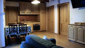 A compact kitchen with wooden cabinets, a dining table with chairs, and a sofa in a living area. - Agriturismo Il regno del marrone (Castel del Rio)
