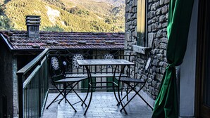 A small outdoor balcony with a table and chairs, a stone wall, and a view of a mountainous landscape. - Agriturismo Il regno del marrone (Castel del Rio)