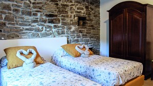 Two beds with floral bedding, a stone wall, and a wooden wardrobe. - Agriturismo Il regno del marrone (Castel del Rio)