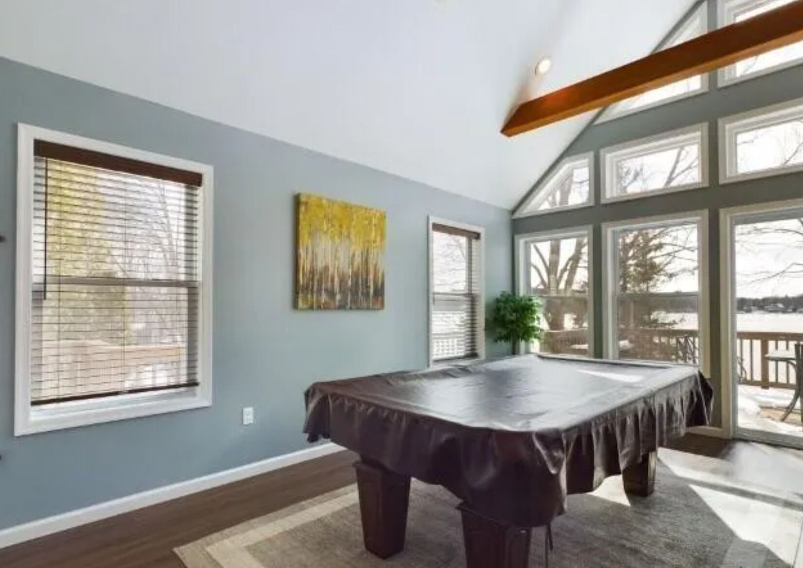 Una habitación con mesa de billar, ventanas amplias y techo con vigas a la vista.