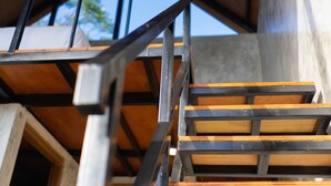 Una escalera con escalones de madera y barandillas de metal en el interior de un edificio con techo alto y ventanal circular.
