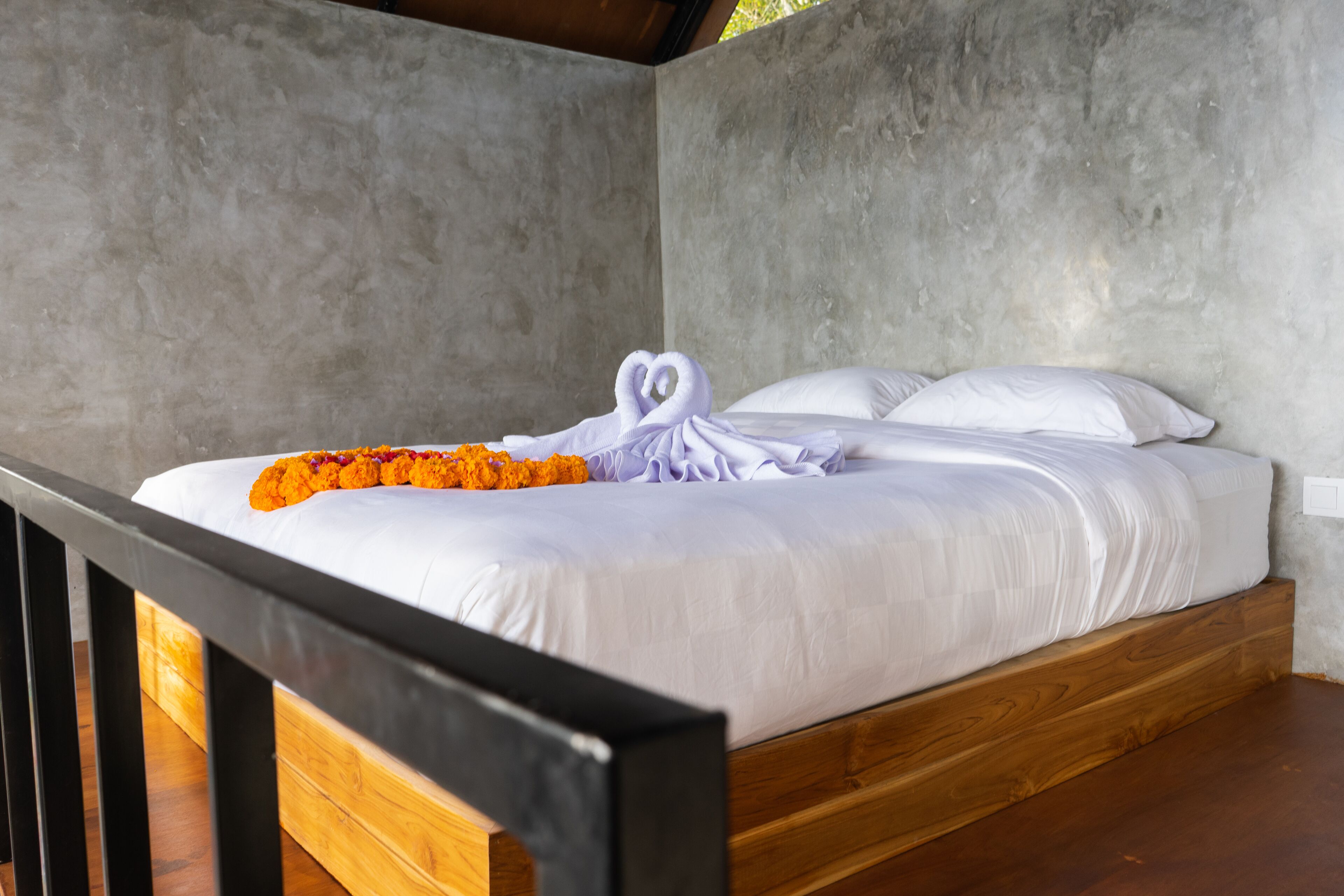 A single bed with white linens, a heart-shaped towel, and orange flowers on the bed.