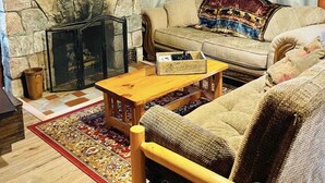 A cozy living room with a stone fireplace, wooden walls, a cushioned sofa, and a coffee table.