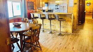 A wooden interior with a bar area, wooden chairs, a dining table, and a kitchen with a microwave and utensils.