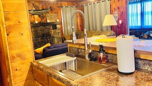 A compact kitchen with wooden cabinetry, a granite countertop, a stainless steel sink, and a dishwasher.