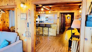 A cozy cabin interior with a wooden floor, a kitchen area with bar stools, and a dining table.