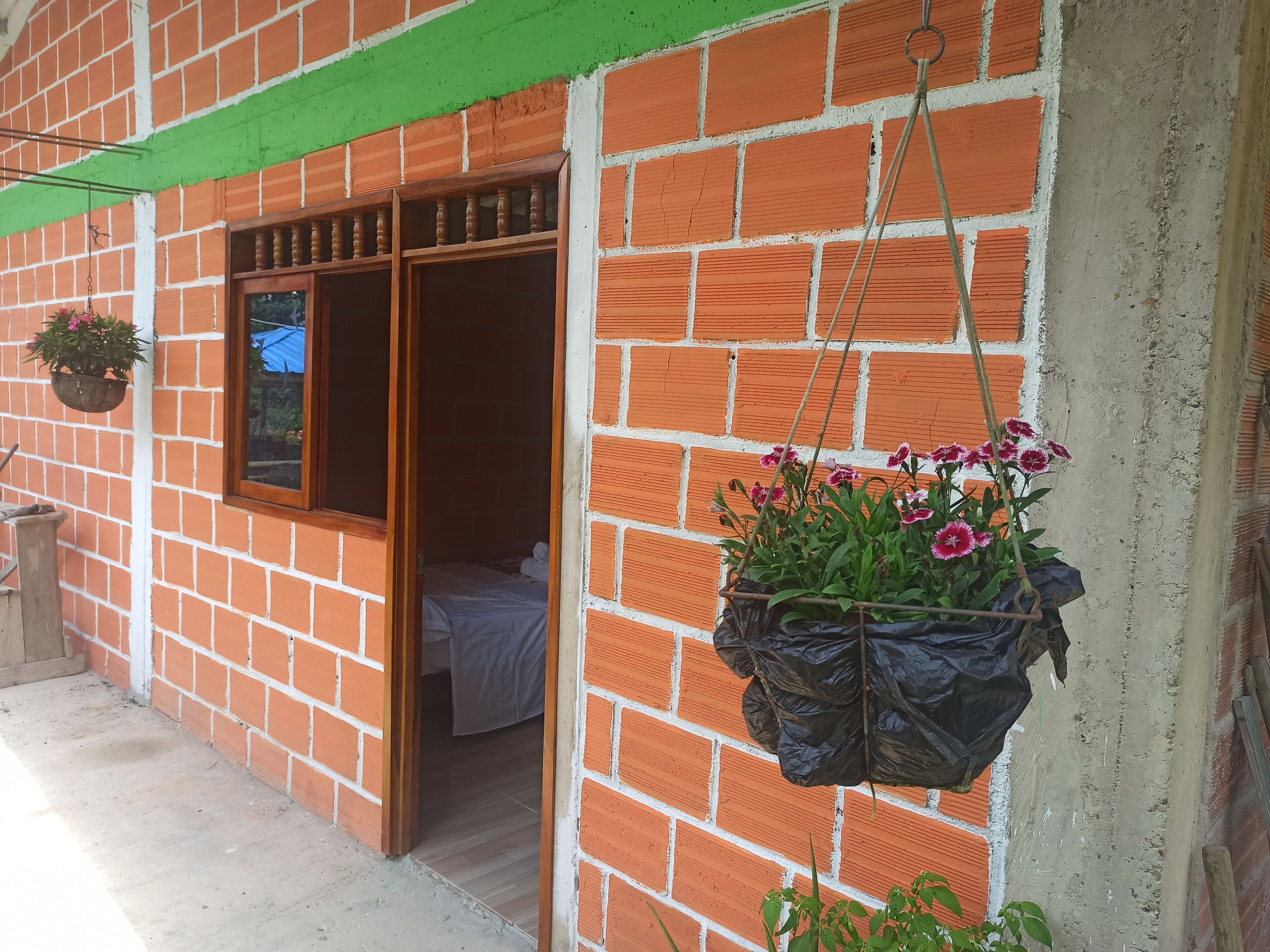 A room with a bed, a window with wooden shutters, and a hanging flower pot.