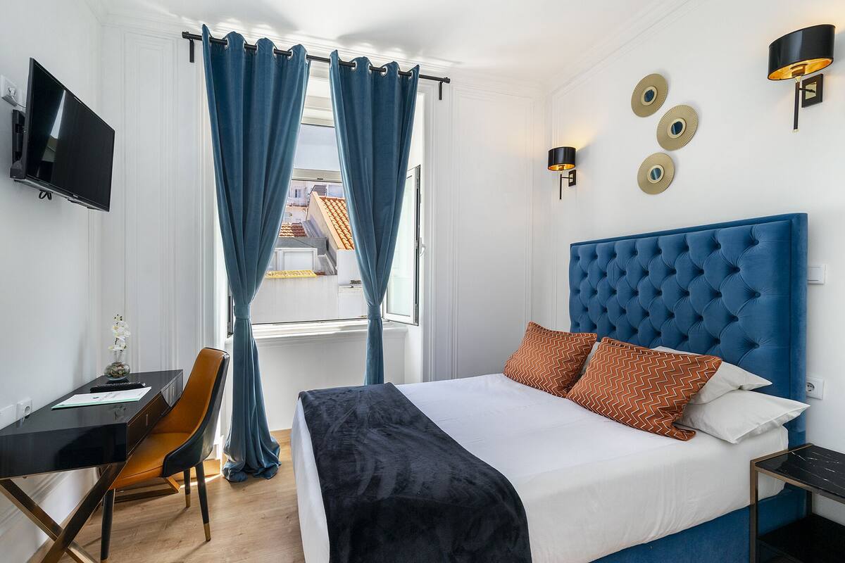 A hotel room with a bed, a desk, a chair, a TV, and a window with curtains.