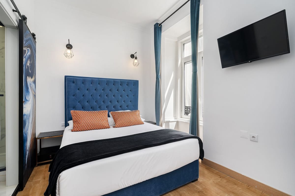 A bedroom with a large bed, two wall-mounted lights, a flat-screen TV, and a window with curtains.